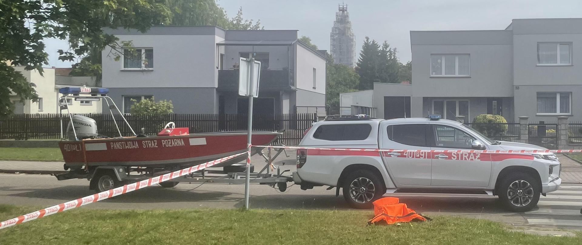 Zdjęcie przedstawia strażaków w działań ratowniczych.
W tle samochód.
