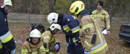 Warszaty szkoleniowe. Zdjęcie przedstawia fragment stadionu w Sarnowie, na którym przygotowane jest stanowisko do "udzielania kwalifikowanej pierwszej pomocy". Na trawie znajduje się torba ze sprzętem do ratownictwa medycznego, szyny Kramera oraz deska ortopedyczna. Obok czterech ćwiczących strażaków, instruktor oraz dwóch obserwatorów. W tle widoczny jest las.