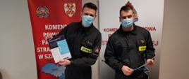 Dwóch umundurowanych strażaków prezentujących ulotki z akcji szczepień przeciwko COVID-19