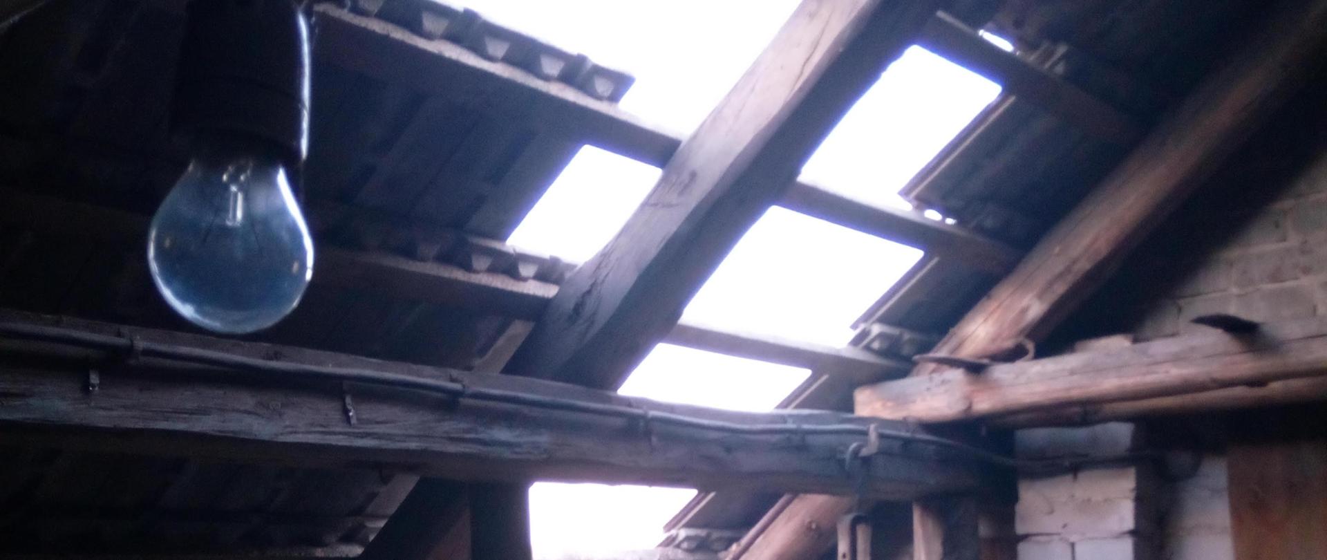 Strych budynku, w którym doszło do wybuchu, widoczna drewniana więźba dachowa z uszkodzonym pokryciem. Brak części pokrycia dachu wykonanego z dachówek, brak około dwudziestu sztuk dachówek bezpośrednio nad otwartym wyłazem na strych.