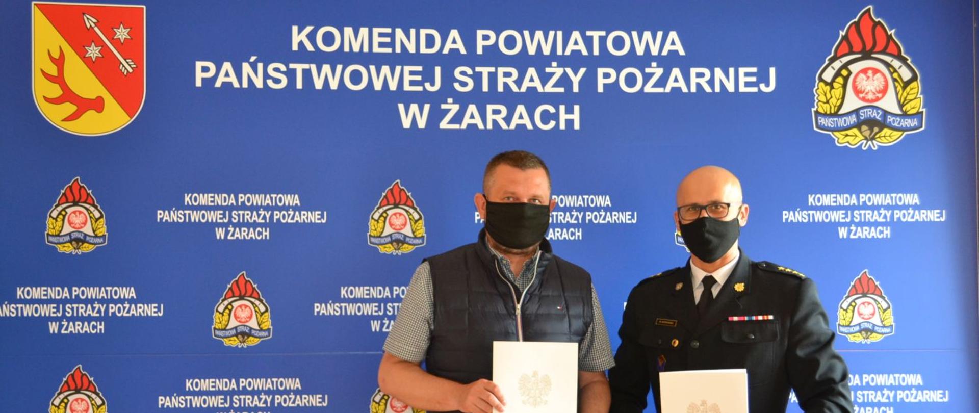 Komendant powiatowy i właściciel firmy budowlanej trzymają w rękach umowę na budowę strażnicy