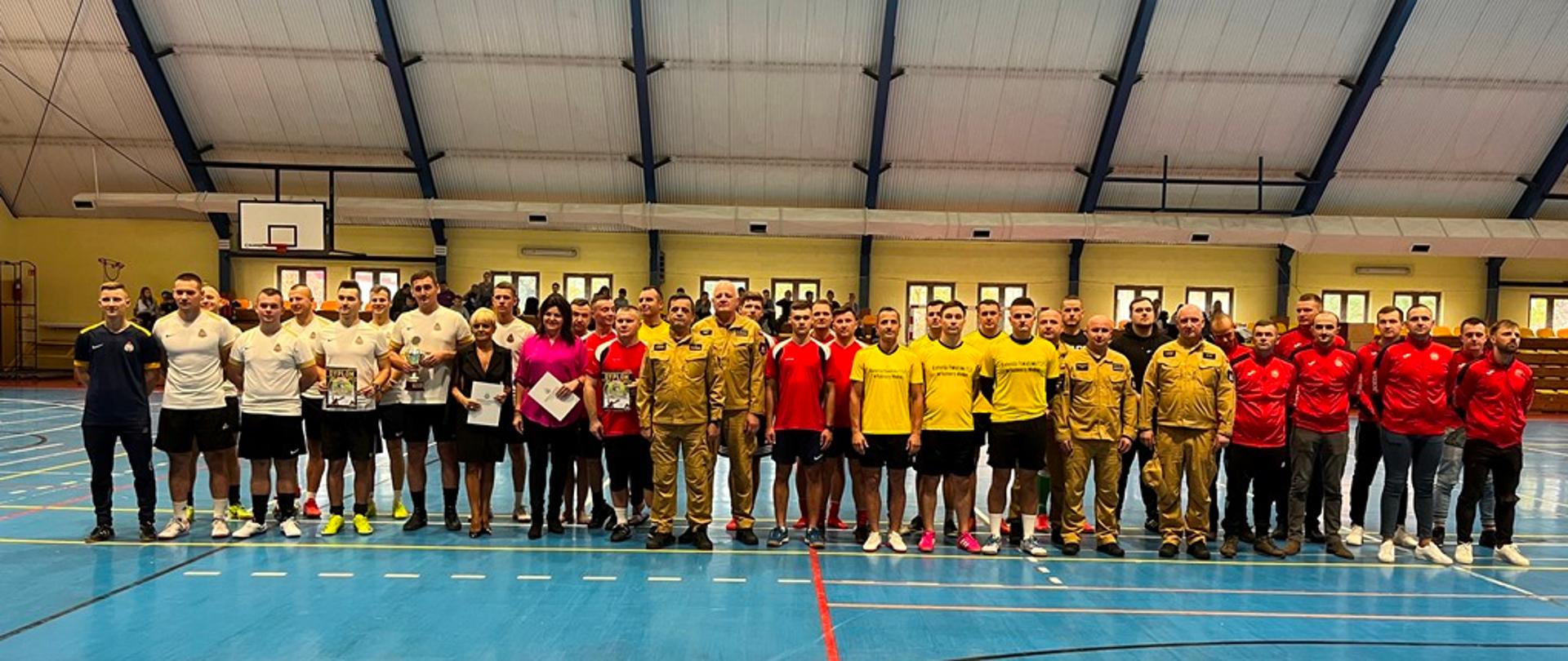 Hala sportowa, zawodnicy wraz z organizatorami pozują w dwuszeregu do zdjęcia. 