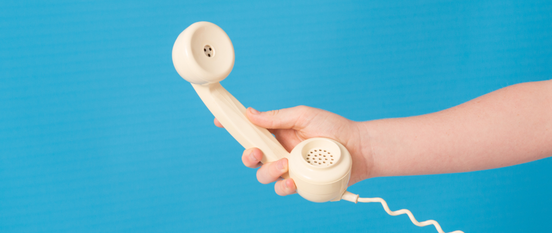 Dłoń trzyma telefon stacjonarny.