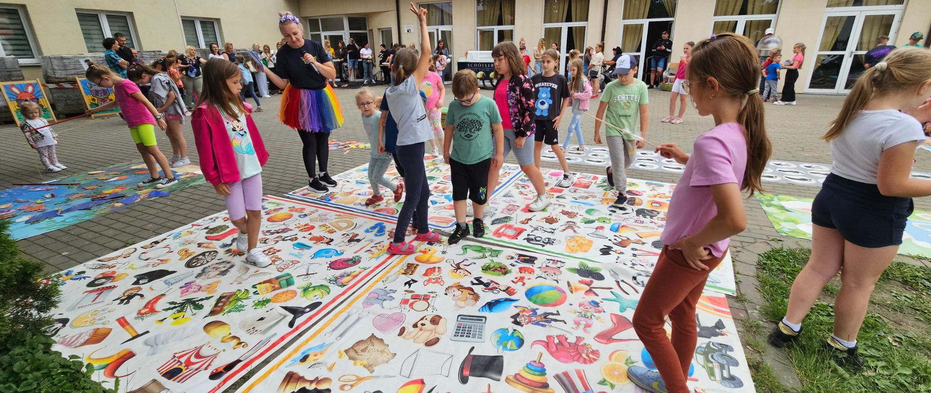 Grupa dzieci stoi na planszach posiadających kolorowe symbole różnych przedmiotów.