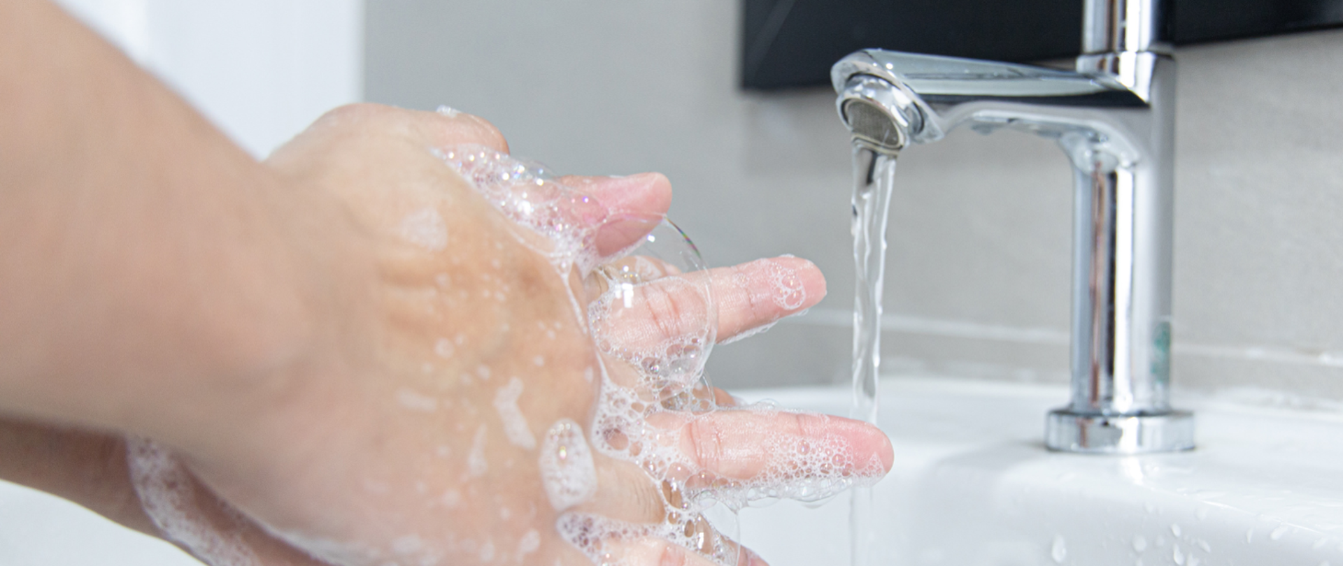 Plakat przedstawiający namydlone dłonie nad umywalką z odkręconą wodą