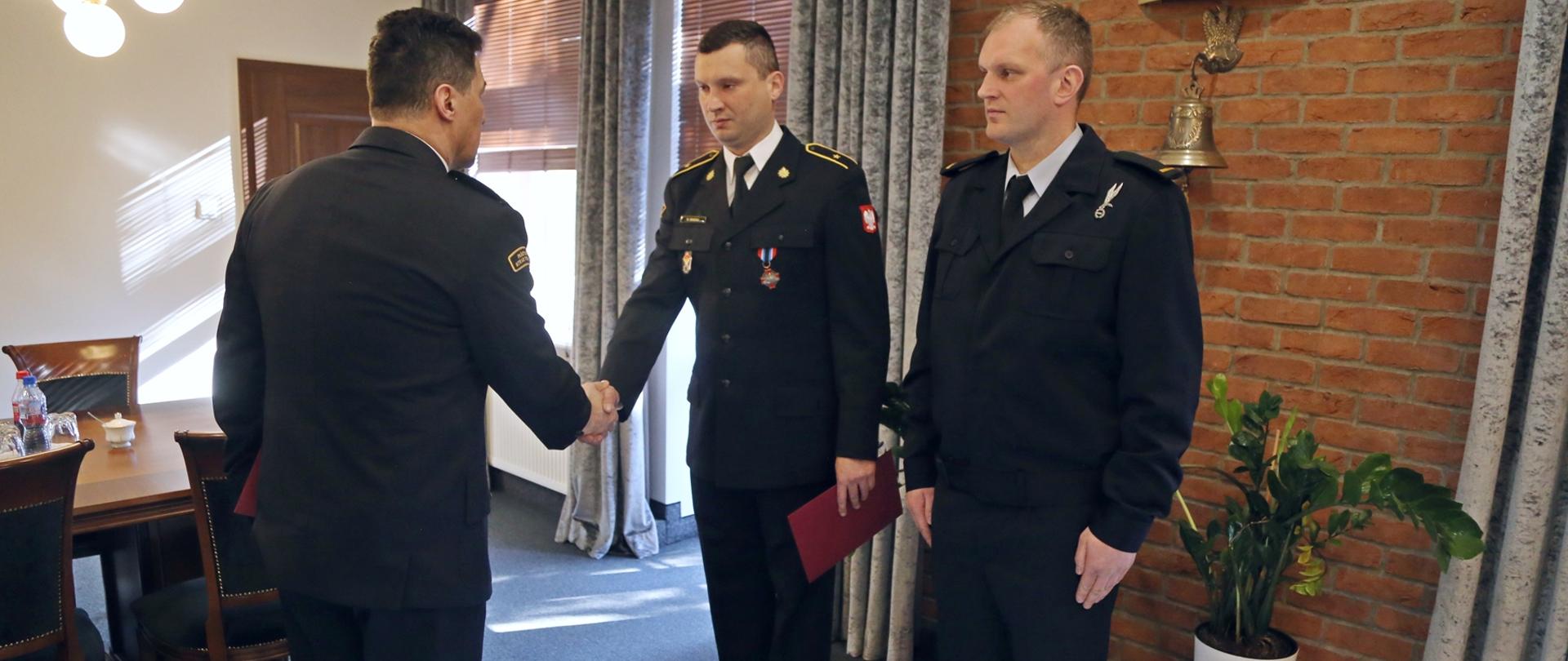 Komendant Centralnej Szkoły gratuluje otrzymanej nagrody jednemu z funkcjonariuszy, obok stojący drugi z nagrodzonych strażaków