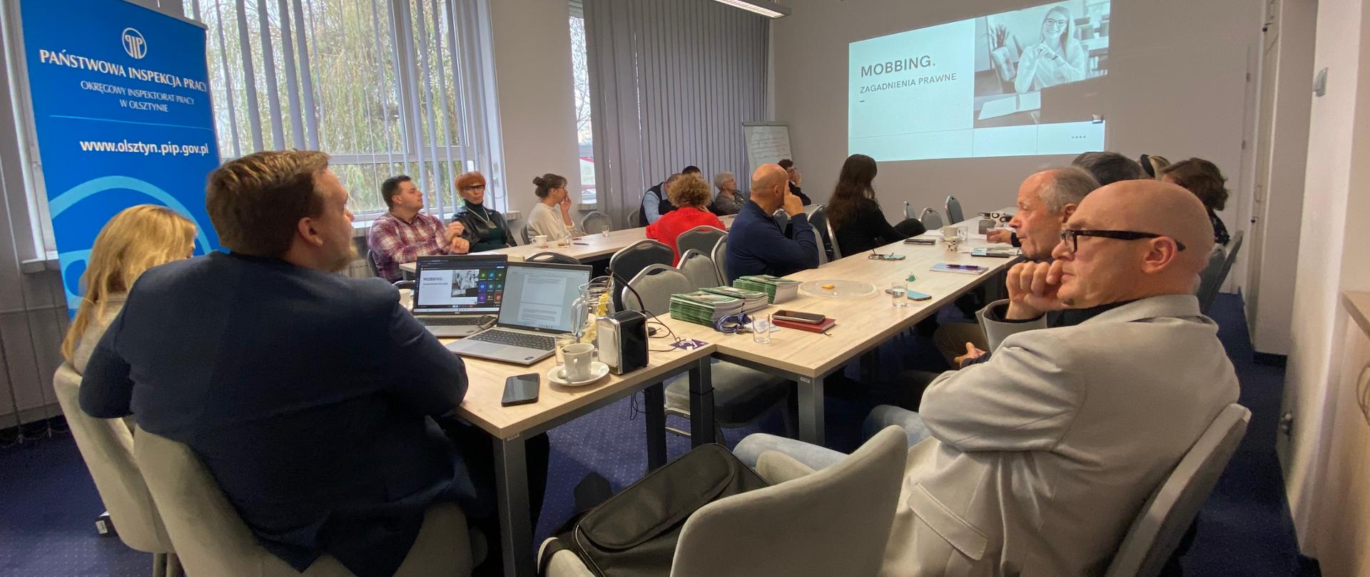 przy stołach ustawionych w lit. U siedzą osoby, w tle slajd Mobbing, zagadnienia prawne