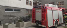 Na zdjęciu widoczny jest samochód pożarniczy, w tle widoczny jest budynek mieszkalny w którym miał miejsce pożar.