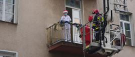Na zdjęciu strażak PSP na podnośniku i lekarz na balkonie.