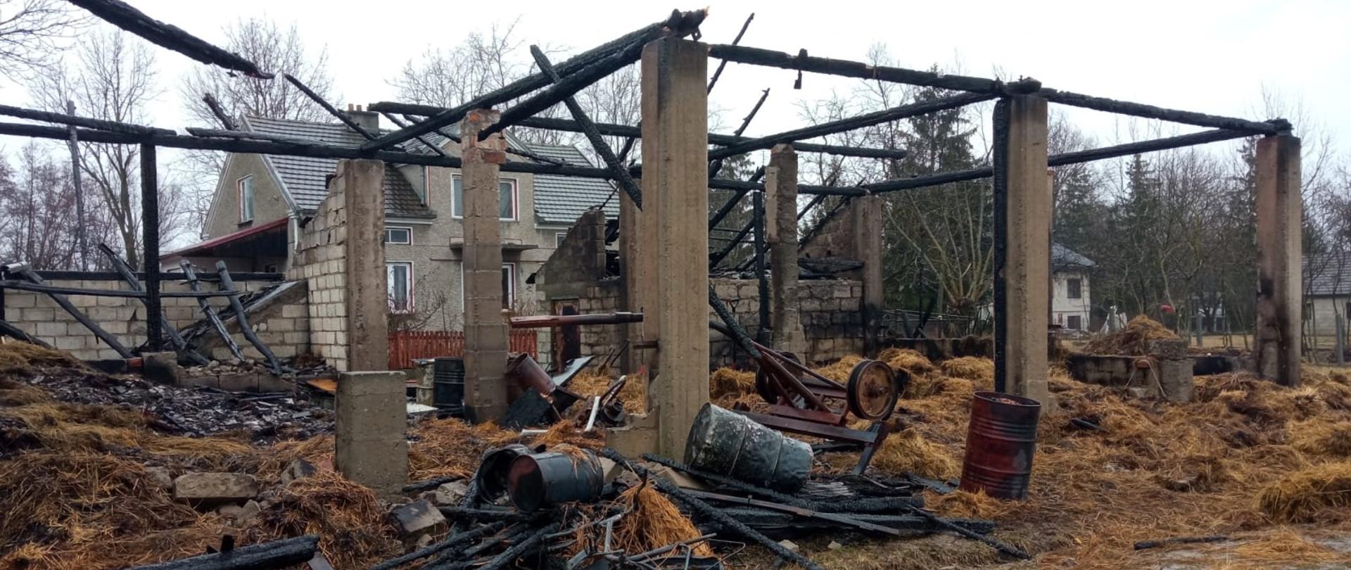 na zdjęciu pozostałości po spalonej stodole wraz z wyposażeniem( beczki stalowe, wóz)