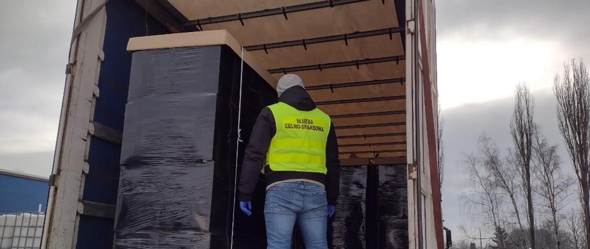 Funkcjonariusz Służby Celno-Skarbowej stoi w naczepie samochodu ciężarowego przed paletami.