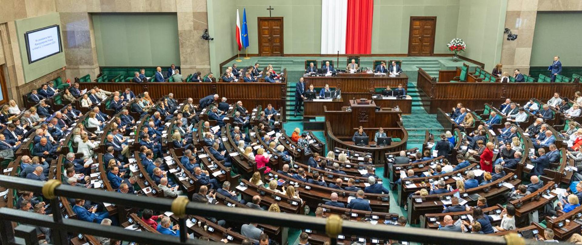 Zdjęcie przedstawia salę plenarną Sejmu RP z siedzącymi w ławach posłankami i posłami. W ławie rządowej po lewej stronie zdjęcia widać premiera Donalda Tuska i członków rządu. Na środku za stołem prezydialnym siedzi marszałek Sejmu Włodzimierz Czarzasty. Za marszałkiem wiszą biało-czerwone barwy narodowe.
