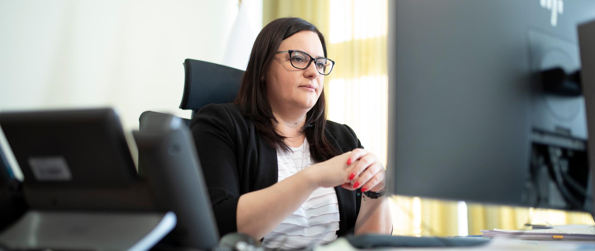 Na zdjęciu wiceminister Małgorzata Jarosińska-Jedynak siedzi przy biurku przed monitorem komputera
