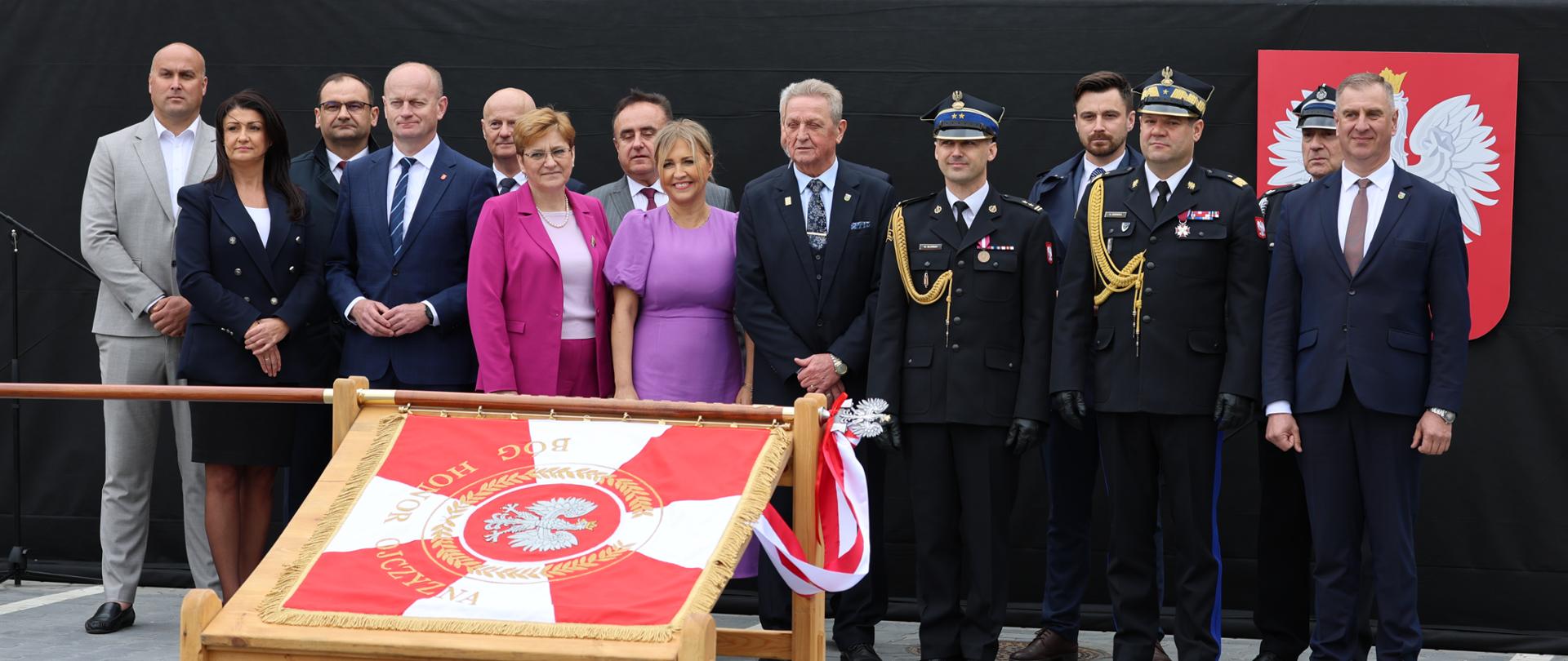 Goście honorowi uroczystości pozują do zdjęcia za sztandarem. 