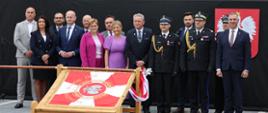 Goście honorowi uroczystości pozują do zdjęcia za sztandarem. 