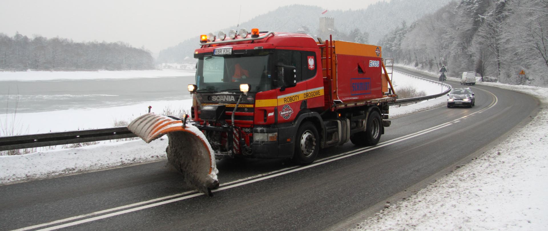 Zimowe utrzymanie DK75, okolice zamku Tropsztyn w woj. małopolskie. Na pierwszym planie pługosolarka pracująca na drodze i zimowy krajobraz.