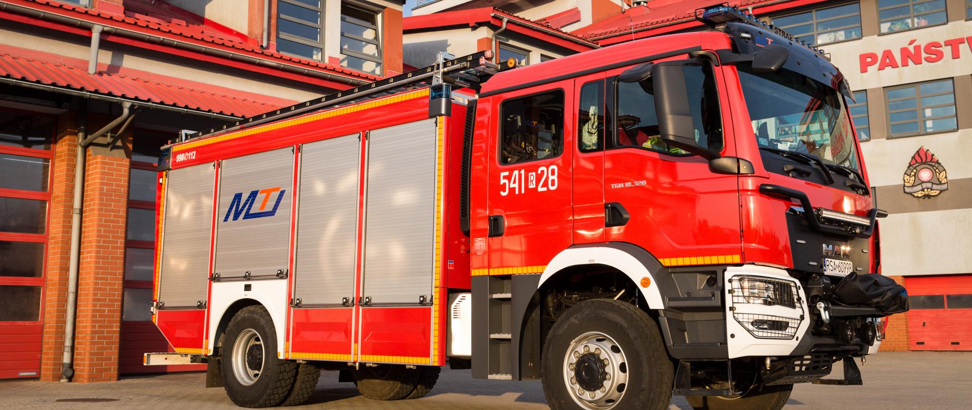 Zdjęcie przedstawia samochód pożarniczy na tle Komendy 