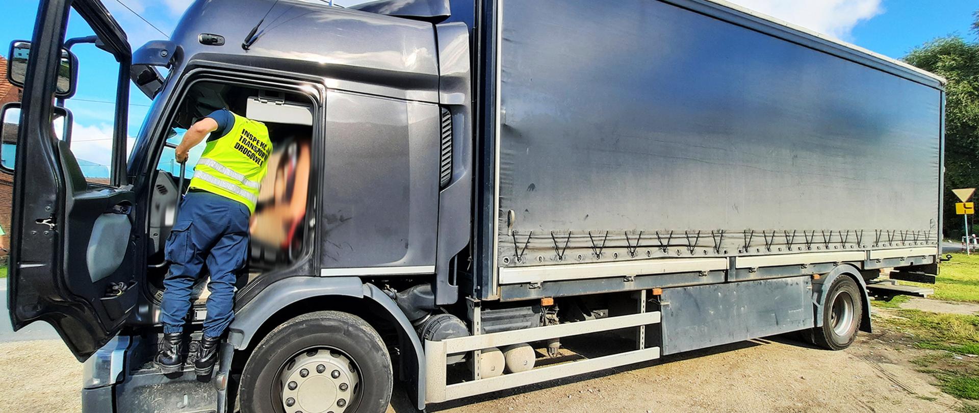 Kontrola inspektorów dolnośląskiej Inspekcji Transportu Drogowego. Na zdjęciu inspektor ITD w kabinie kierowcy pobiera dane o czasie pracy kierowcy samochodu ciężarowego. Pojazd kurierski stoi zaparkowany przy jednej z lokalnych ulic.