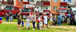 Na zdjęciu dzieci z rodzicami na tle samochodów pożarniczych PSP. W tle bloki mieszkalne