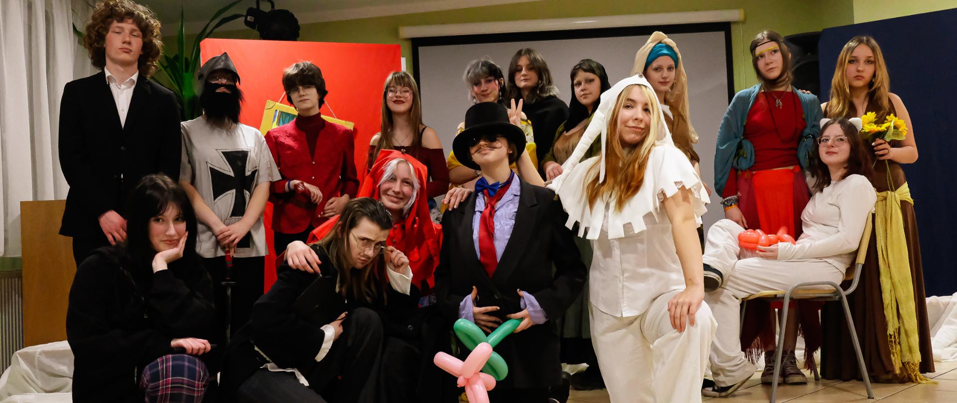 Zdjęcie przedstawia wszystkich aktorów - uczniów biorących udział w przedstawieniu z okazji Balu Matejkowskiego, na pierwszym planie postać ubrana w biały strój Stańczyka.