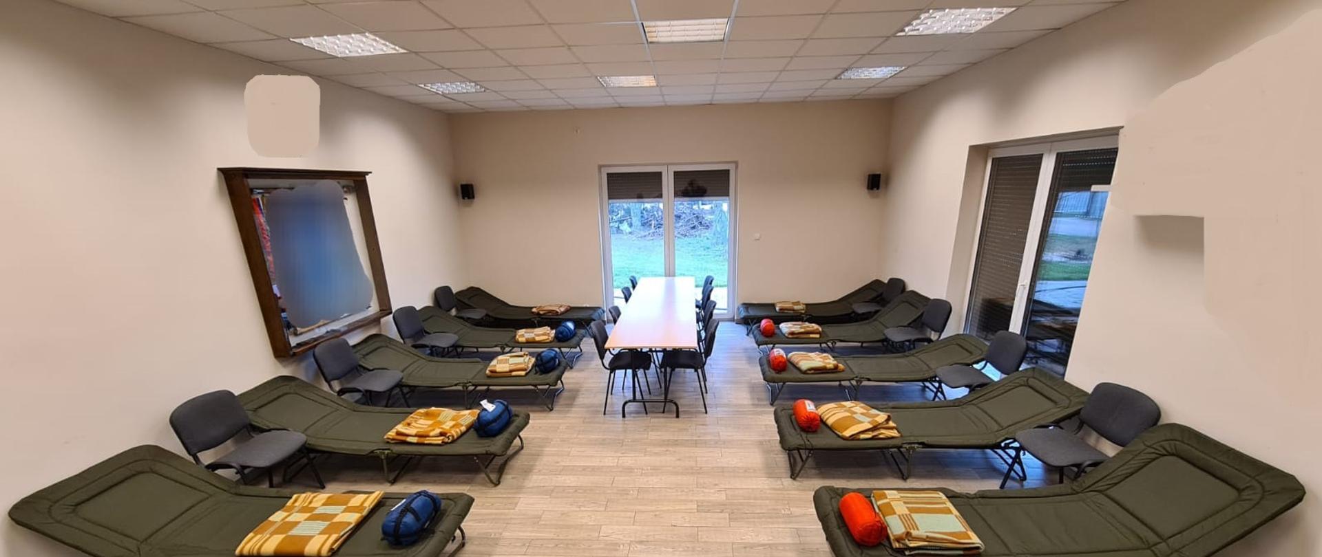 Widać przygotowane miejsce noclegowe na świetlicy, są łózka, stoły, krzesła