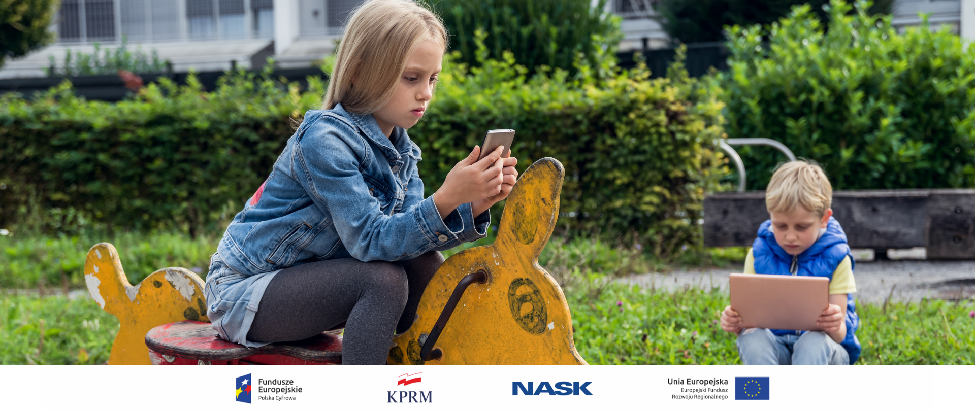 Dwoje dzieci - chłopiec i dziewczynka - na placu zabaw, siedzą na huśtawkach. Dziewczynka (na pierwszym planie) wpatrzona w ekran smartfona, chłopiec - w tableta.