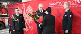 Pani w czarnym ubraniu wręcza strażakowi kwiaty. 