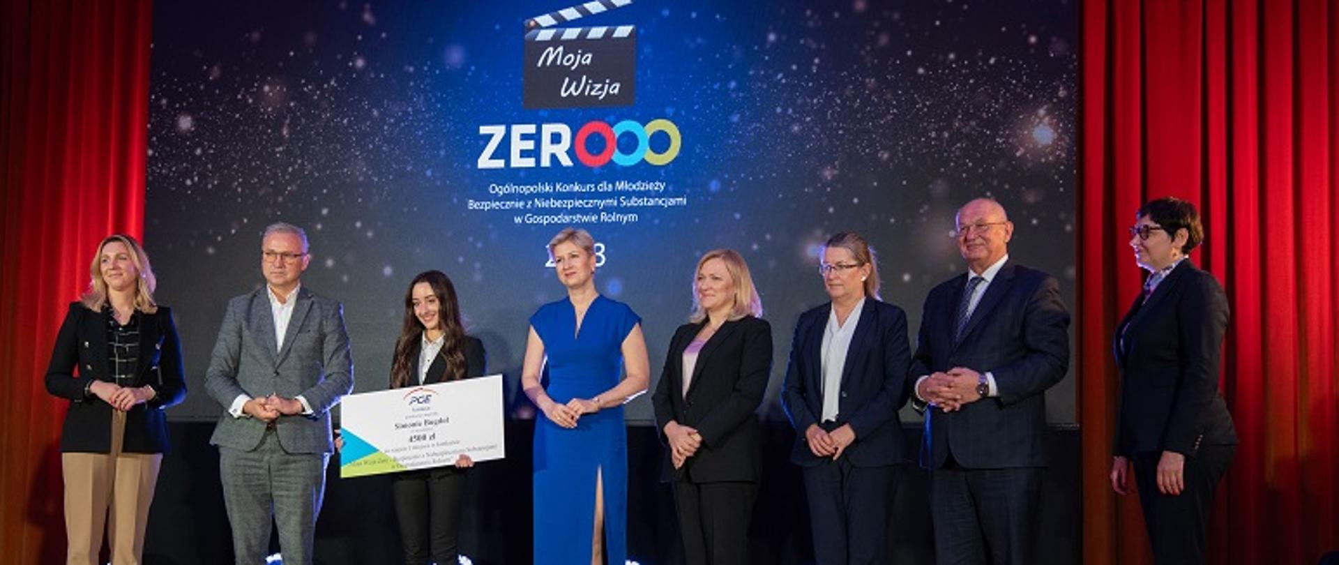 Laureatka I miejsca w Konkursie Moja Wizja Zero stoi na scenie w gronie Organizatorów z czekiem i nagrodami 