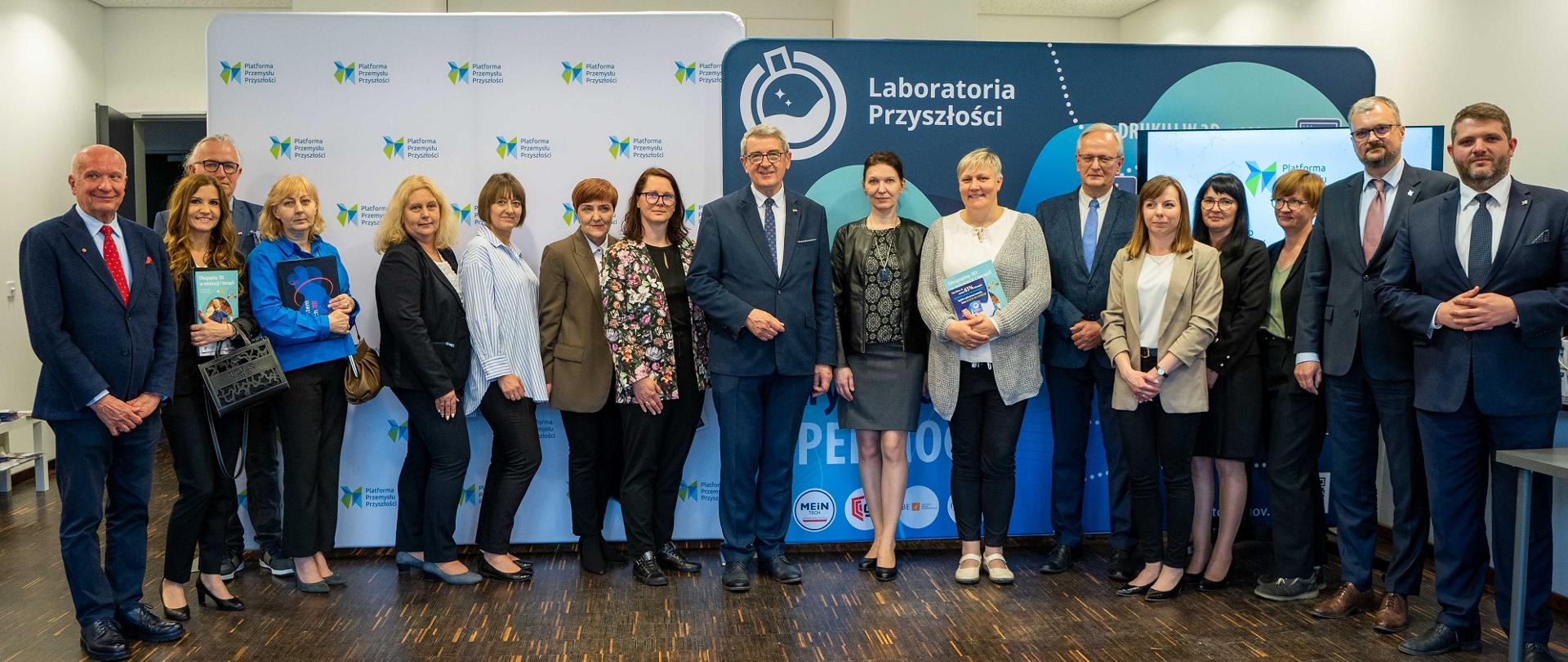 Zdjęcie zbiorowe, w dużej sali pod ścianką z napisem Laboratoria Przyszłości stoi grupa kilkunastu osób.