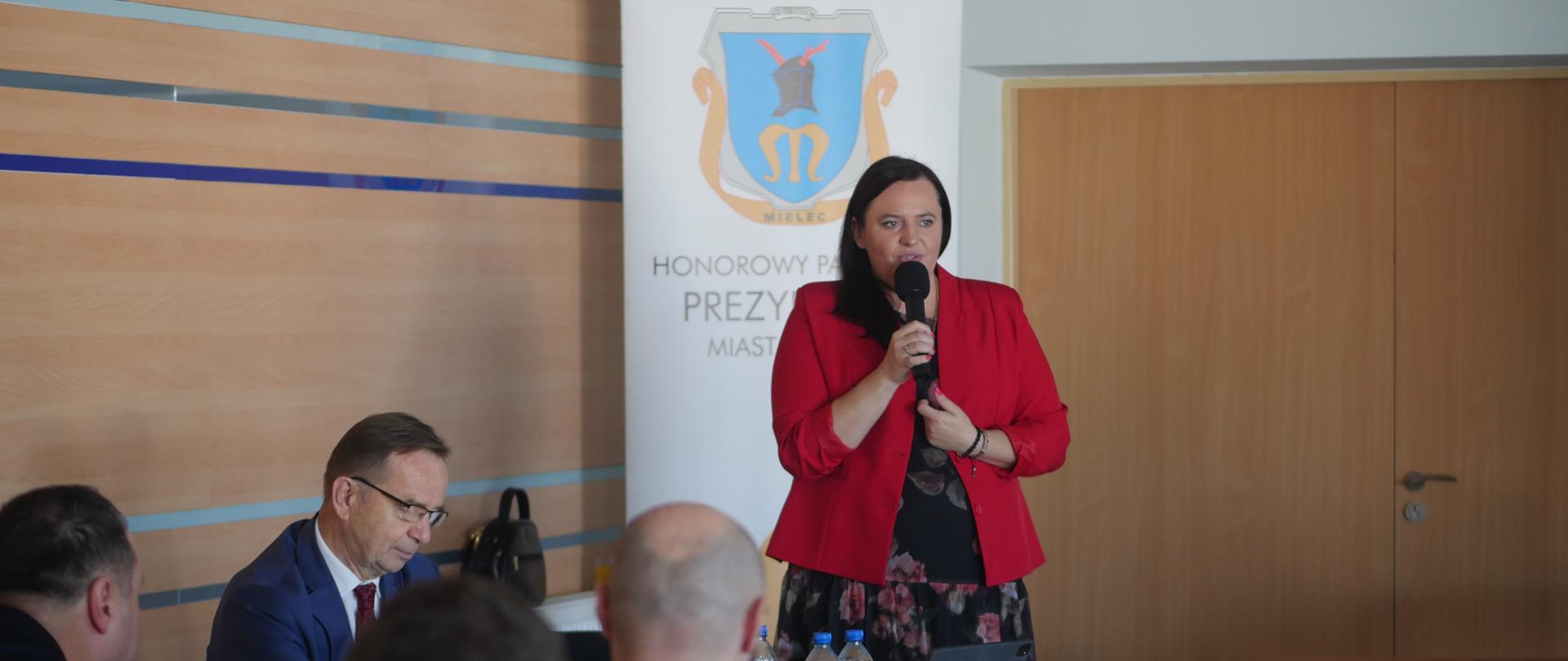 wiceminister Małgorzata Jarosińska-Jedynak mówi do mikrofonu, uczestnicy siedzą na sali
