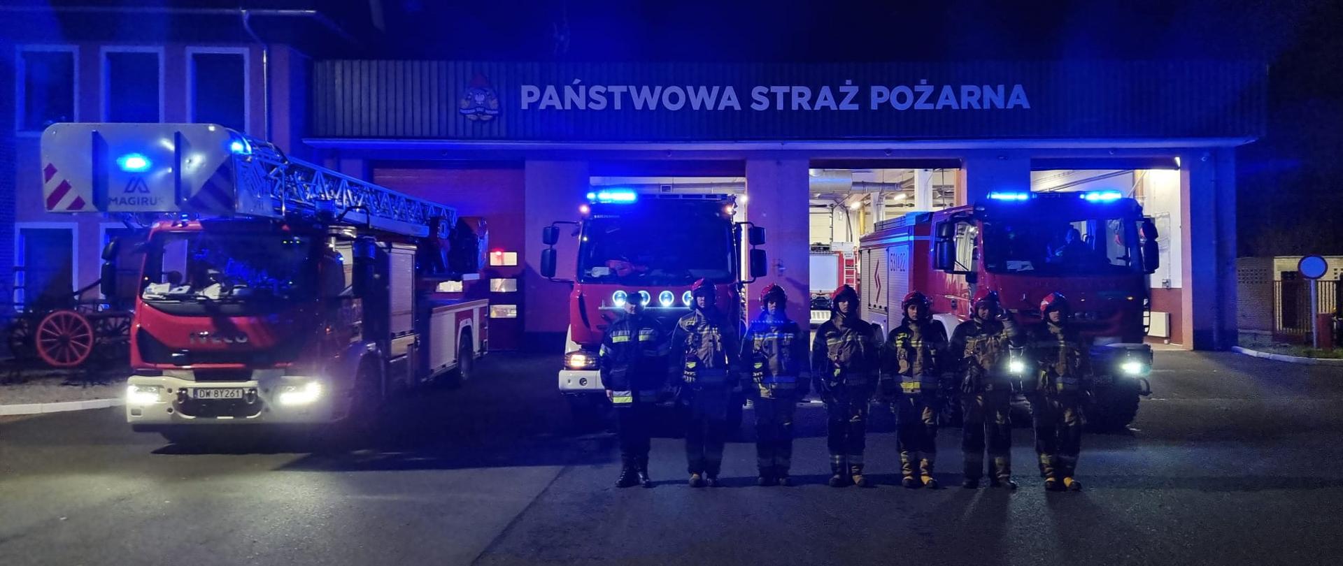 JRG Polkowice w hołdzie ofiarom wypadku. Strażacy JRG Polkowice na tle pojazdów pożarniczych.