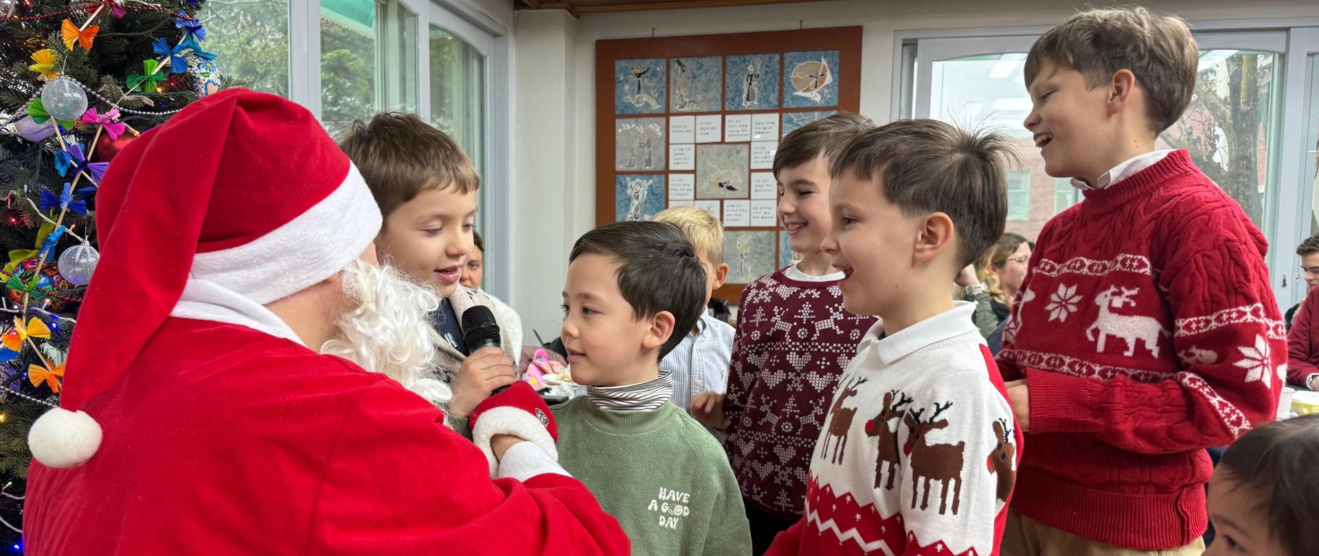 Zdjęcie przedstawia zgromadzone przy choince dzieci, odpowiadające na pytania siedzącego Świętego Mikołaja, w ramach konkursu wiedzy o polskich tradycjach bożonarodzeniowych.