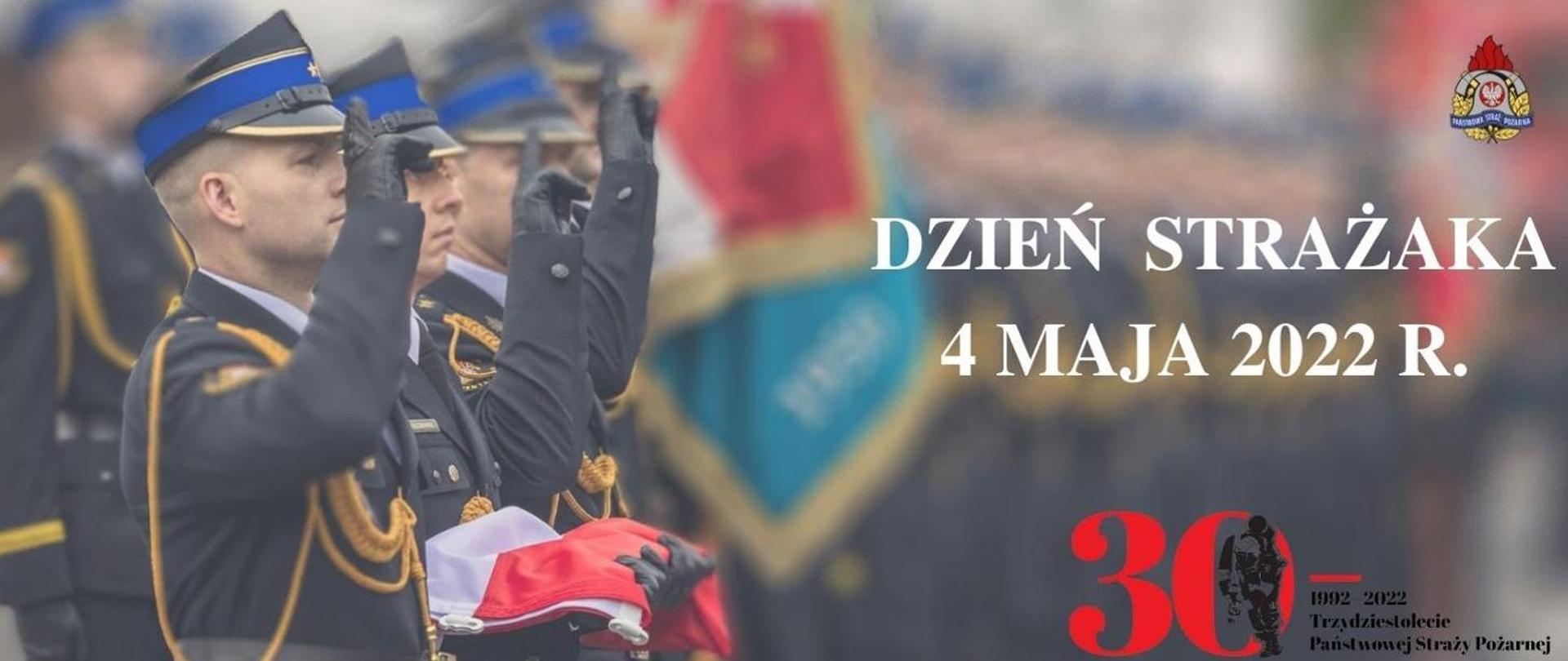 Zdjęcie przedstawia sylwetki strażaków w umundurowaniu galowym podczas salutowania. Jeden z nich trzyma w rękach złożoną flagę Polski. Obok widnieje napis: DZIEŃ STRAŻAKA 4 MAJA 2022 R. oraz logo 30-lecia Państwowej Straży Pożarnej oraz Państwowej Straży Pożarnej.