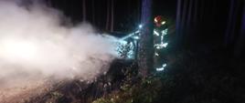Strażak gasi palący się samochód osobowy na drodze leśnej. Samochód uległ całkowitemu zniszczeniu w wyniku pożaru.