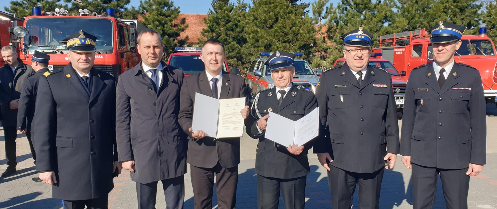 Oficerowie Państwowej Straży Pożarnej wraz z przedstawicielami władz oraz prezesem Ochotniczej Straży Pożarnej w Łazach z promesą na zakup nowego samochodu ratowniczo-gaśniczego dla OSP Łazy.
