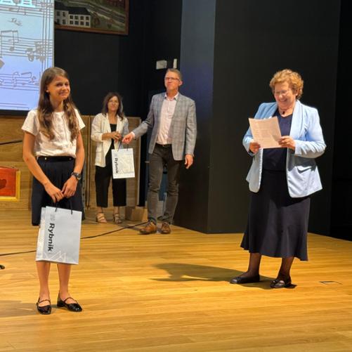 Na scenie stoi dziewczynka i kobieta, za nimi w tle kobita i mężczyzna.