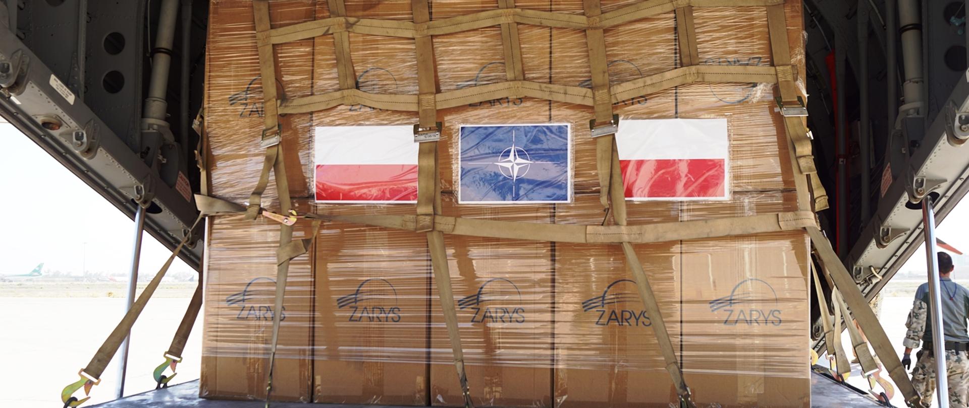 Pudełka zapakowane we wnętrzu samolotu z flagą Polski i symbolem NATO