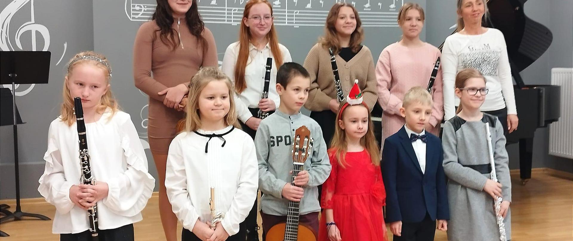 Zdjecie przedstawia uczniów w auli szkoły trzymajacych instrumenty.
