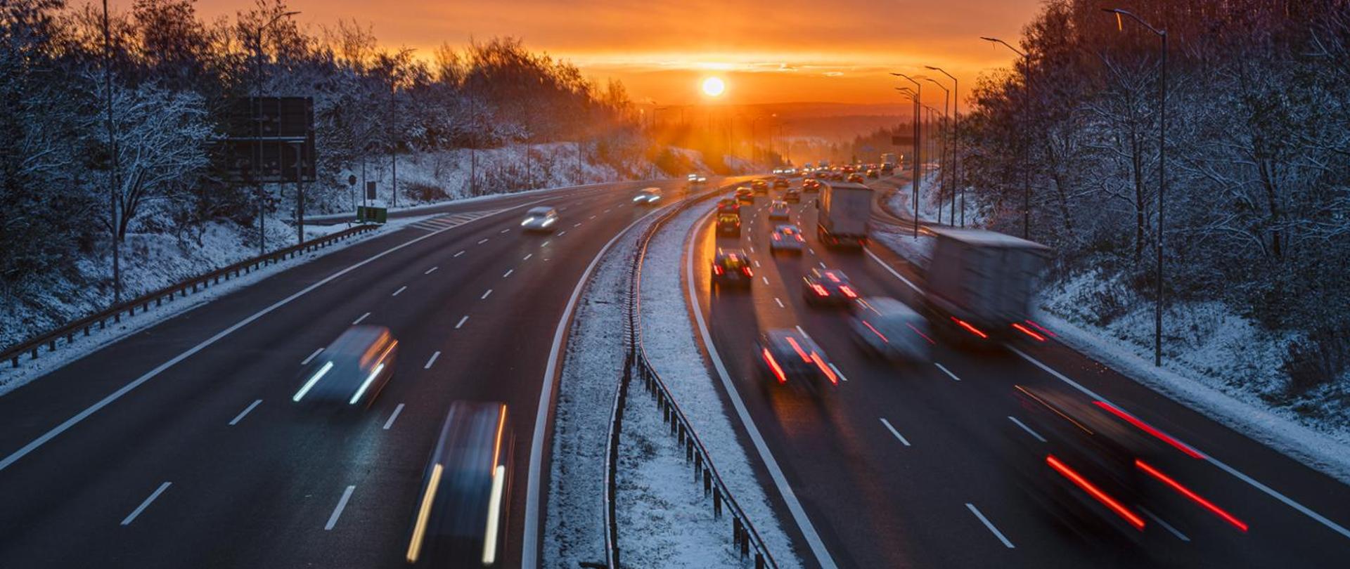 Droga szybkiego ruchu w zimie, w oddali słońce, po obu stronach drogi ośnieżony las