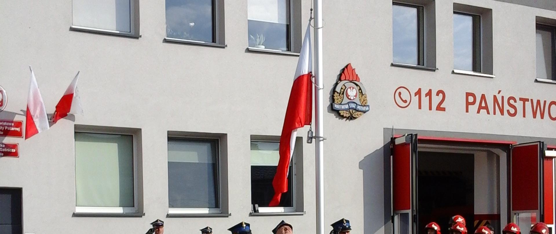 Na zdjęciu widać strażaków przed Komendą Powiatowa PSP w Kolnie w trakcie zmiany służby dokonano uroczystego podniesienia flagi państwowej na maszt przez poczet flagowy przy asyście dwóch zmian służbowych. W uroczystym podniesieniu flagi uczestniczył Komendant Powiatowy PSP w Kolnie st. bryg. Paweł Pupek.