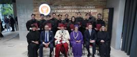 Zdjęcie zbiorowe, na krzesłach ustawionych w szereg siedzi sześc osób, drugi od lewej minister Kulasek, obok niego mężczyzna w czerwonym ceremonialnym stroju, za nimi stoi rząd jedenastu osób w czarnych ubraniach, za nimi ściana z napisem filia Uniwersytetu w Białymstoku w Wilnie.