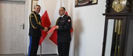 st. bryg. Henryk Koźlewicz odbiera akt powołania od nadbryg. Piotra Socha - Pomorskiego Komendanta Wojewódzkiego PSP. W tle flagi Polski oraz wiszące na ścianie szable.