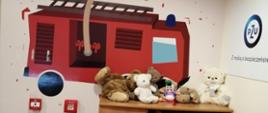 Zdjęcie przedstawia wnętrze sali edukacyjnej Ognik. Na ścianach rysunkowy samochód pożarniczy. Widoczna szafka z pluszakami i stolik