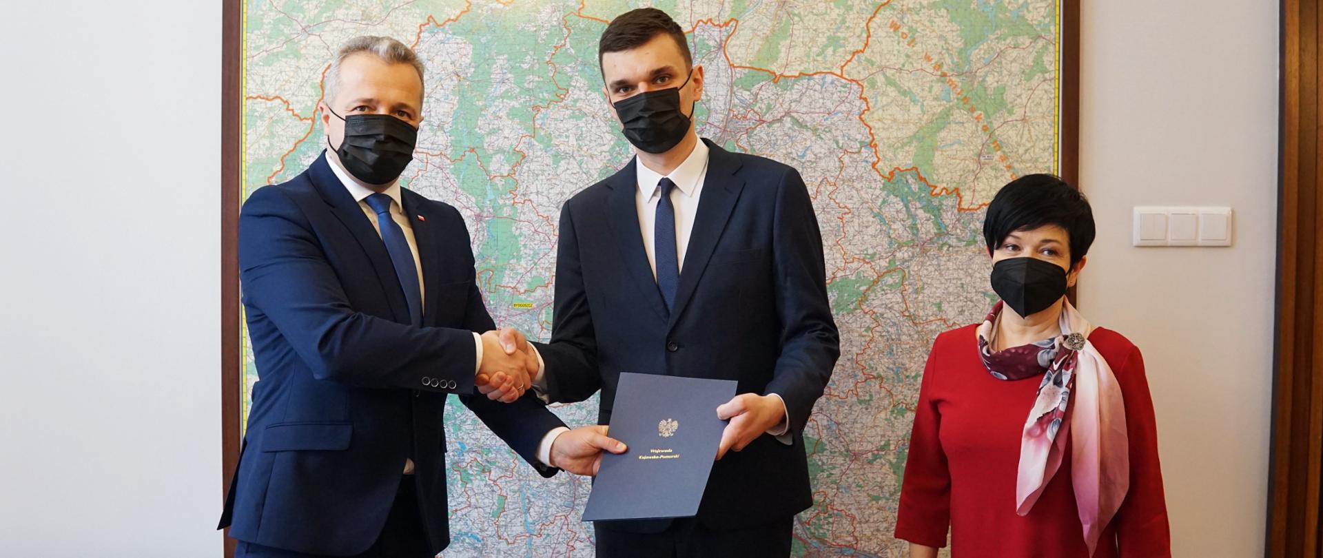 Trzy osoby stojące na tle mapy województwa kujawsko-pomorskiego