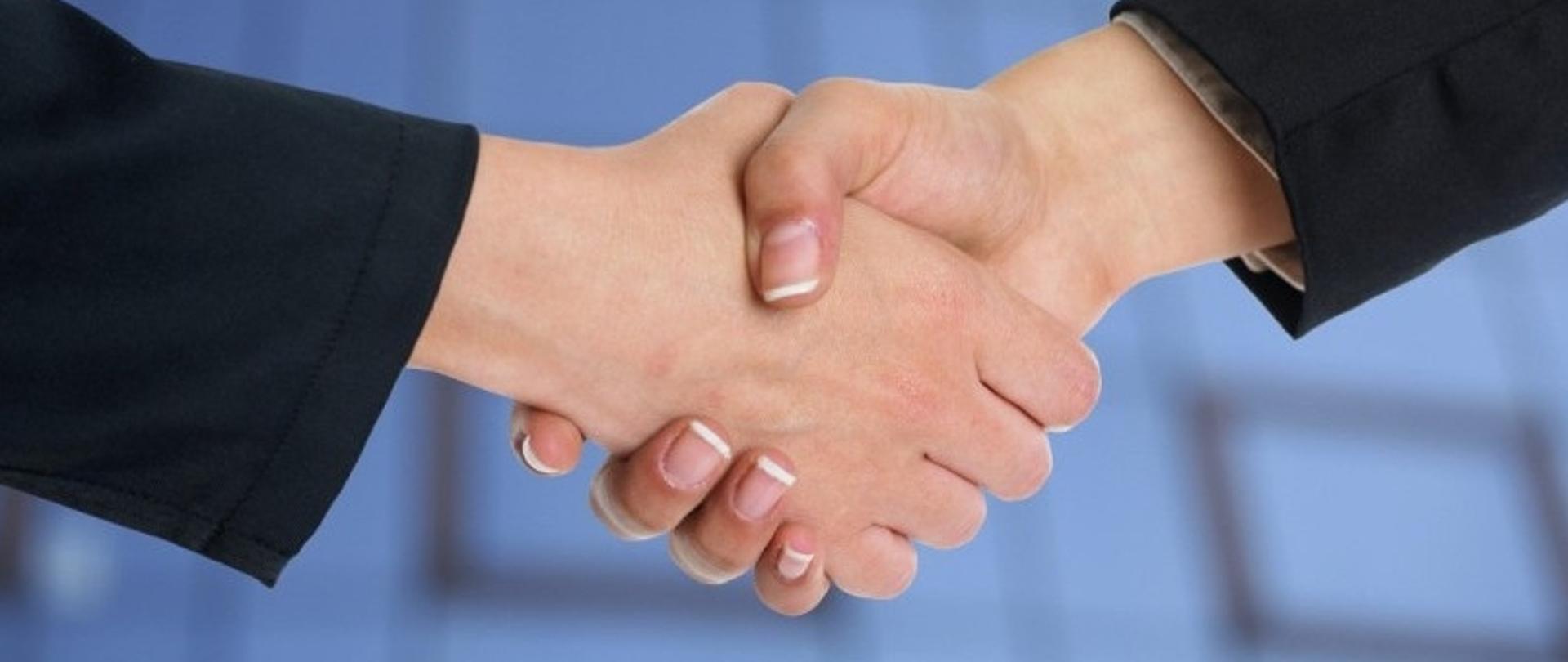 Uścisk dłoni dwóch osób w garniturach na tle niebieskiego tła 