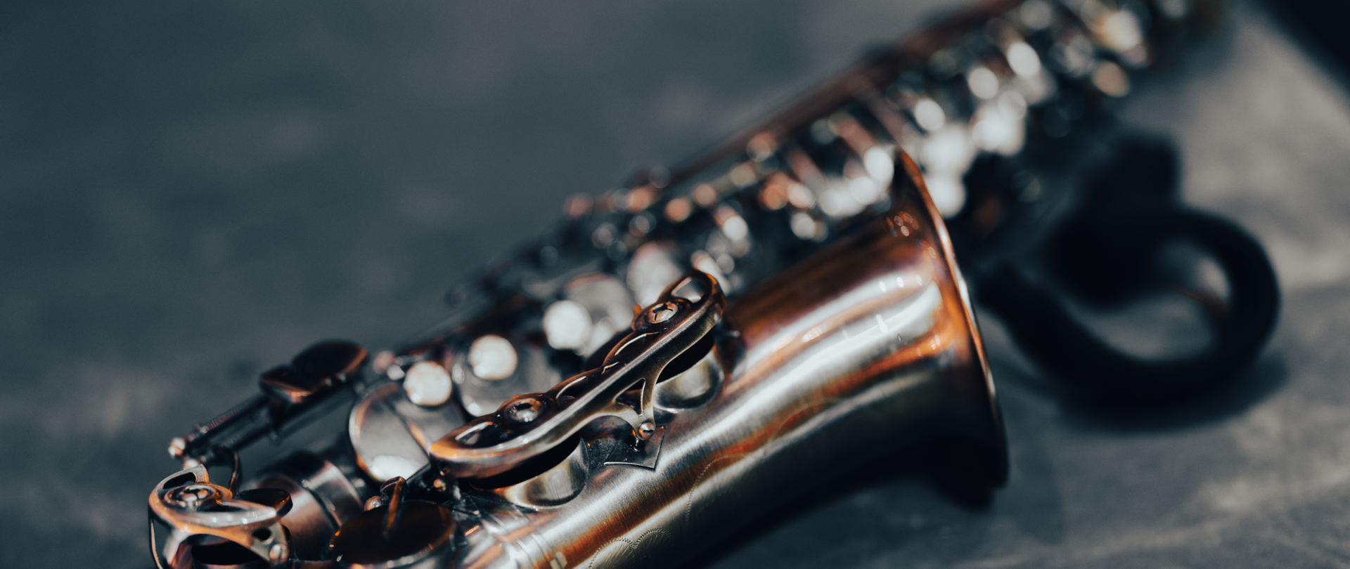 Saksofon w kolorze srebrno-miedzianym z lekko rozmazanym czarnym tłem leżący na stoliku