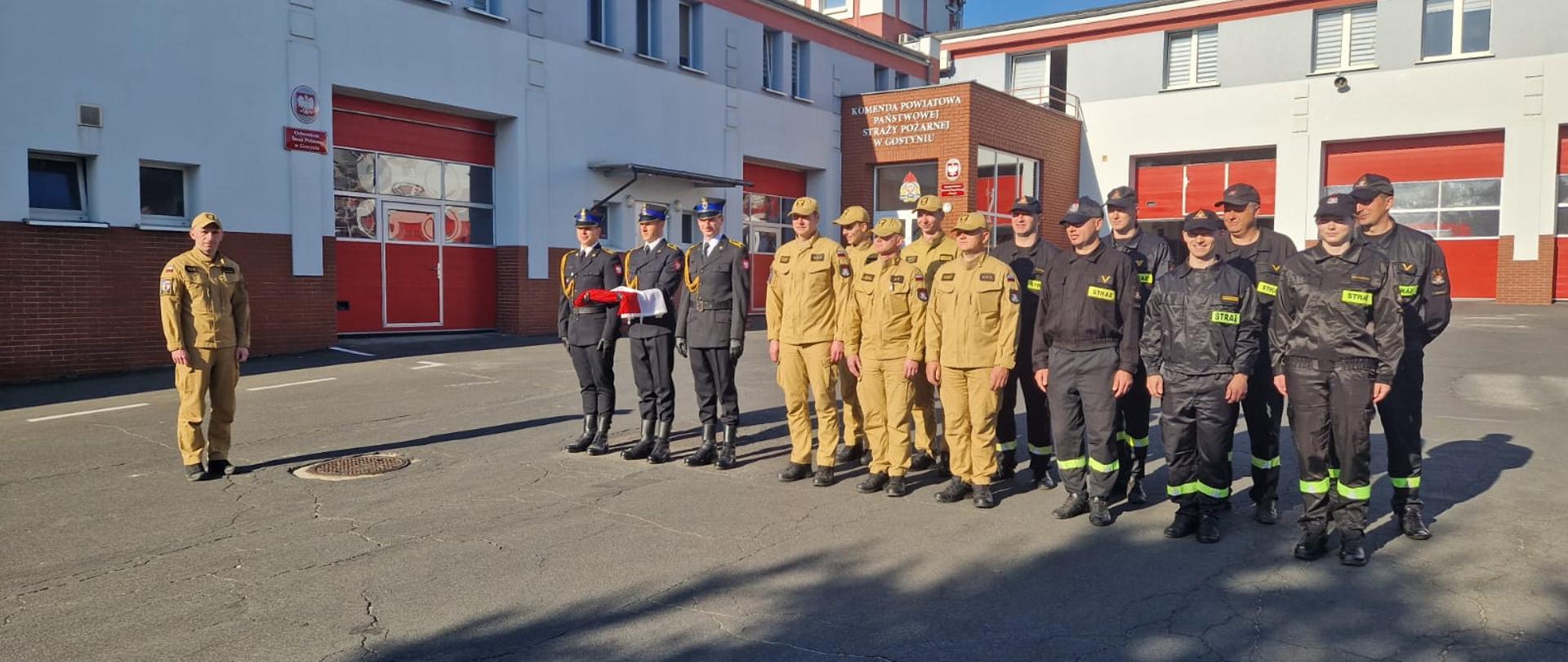 Strażacy stoją na placu komendy podczas zbiórki. W składu pododdziału wchodzi także poczet flagowy.