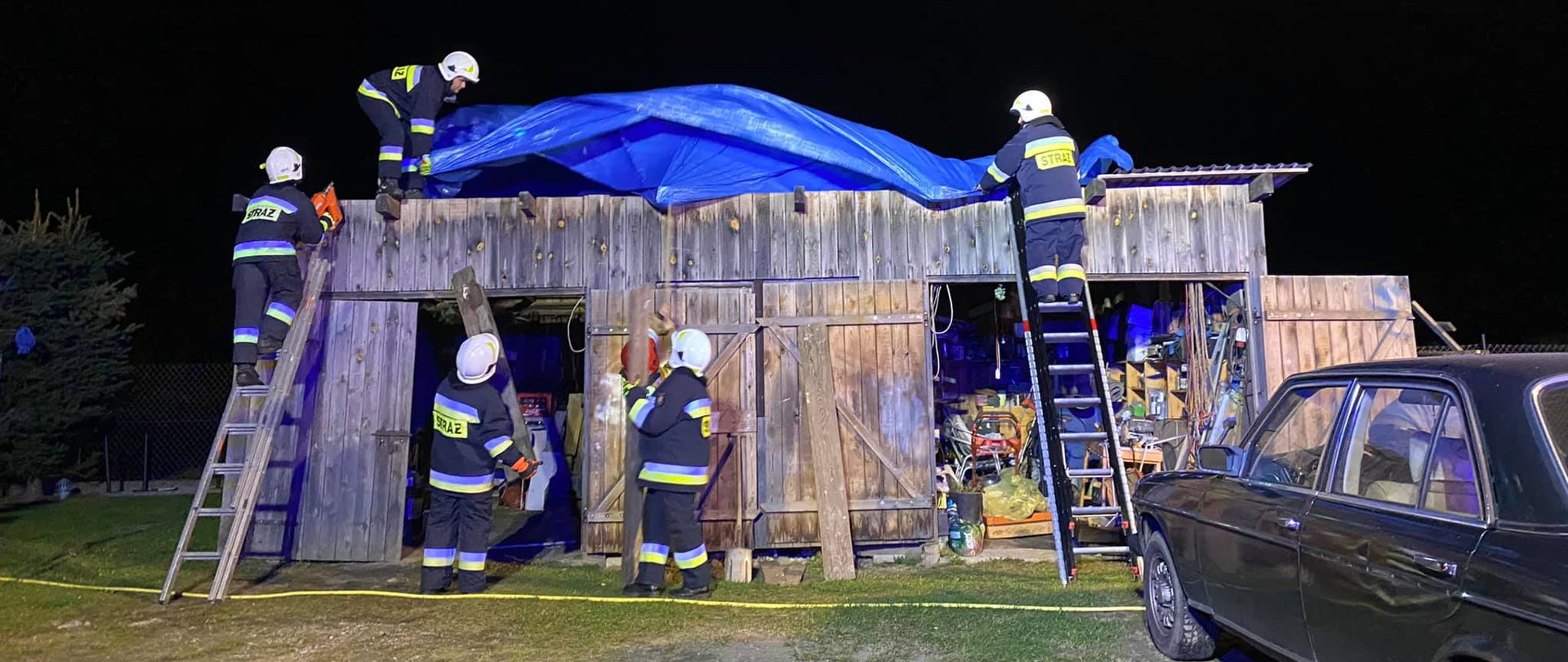 Zdjęcie przedstawia strażaków zabezpieczających budynek gospodarczego, po zerwaniu dachu przez wiatr.
