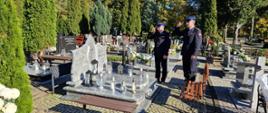 Strażacy oddają honory przed grobem zmarłego funkcjonariusza, na grobowcu znicze 