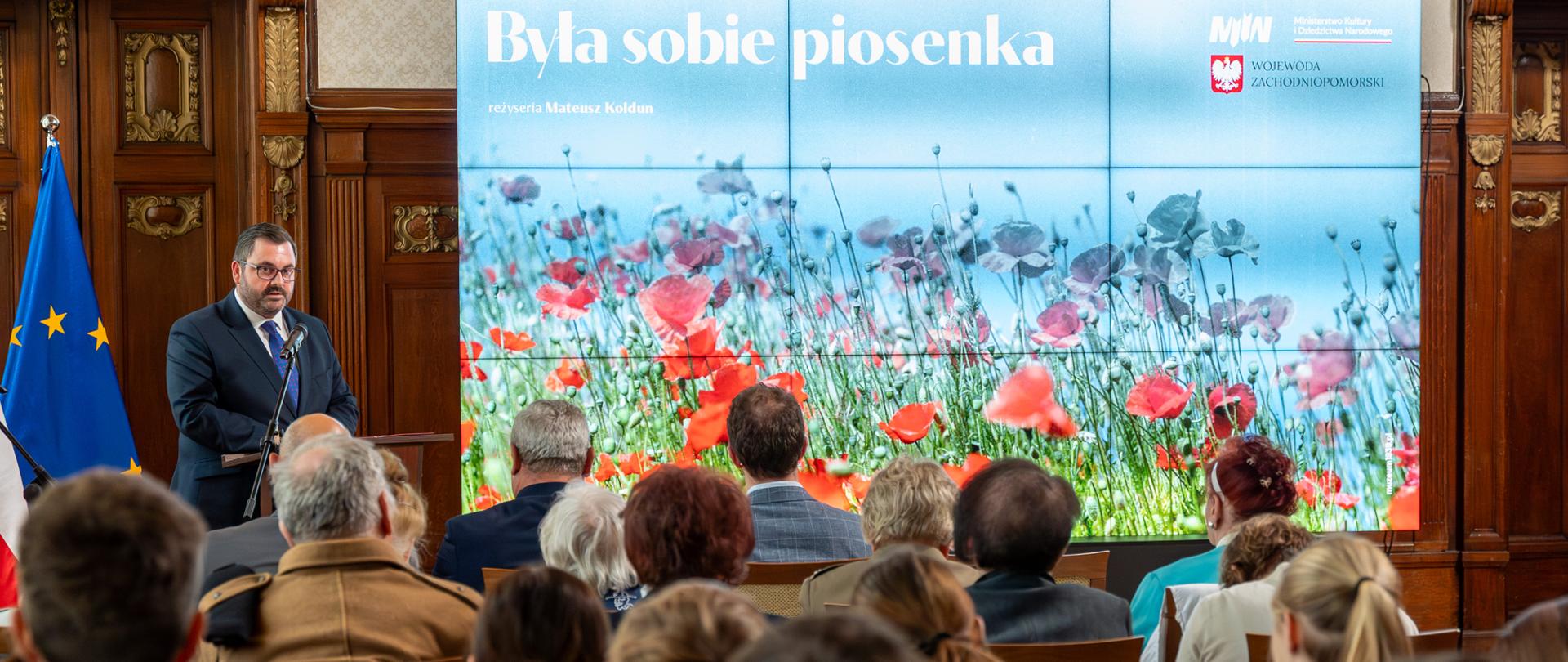 widok na ekran oraz przemawiającego zza pleców uczestników pokazu filmu